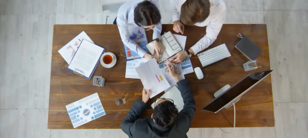 Overhead view of a diverse business team collaborating around a wooden table, analyzing charts, graphs, and documents.