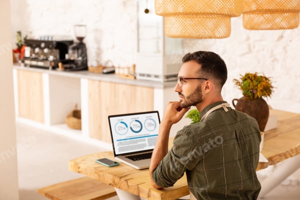 Business owner sitting in his coffee shop while working online on a laptop